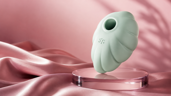 Stimulateur deux-en-un posé sur un socle de verre, fond de satin rose