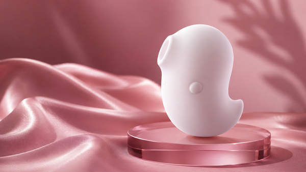 Stimulateur lay-on en silicone blanc posé sur un socle de verre, fond de satin rose